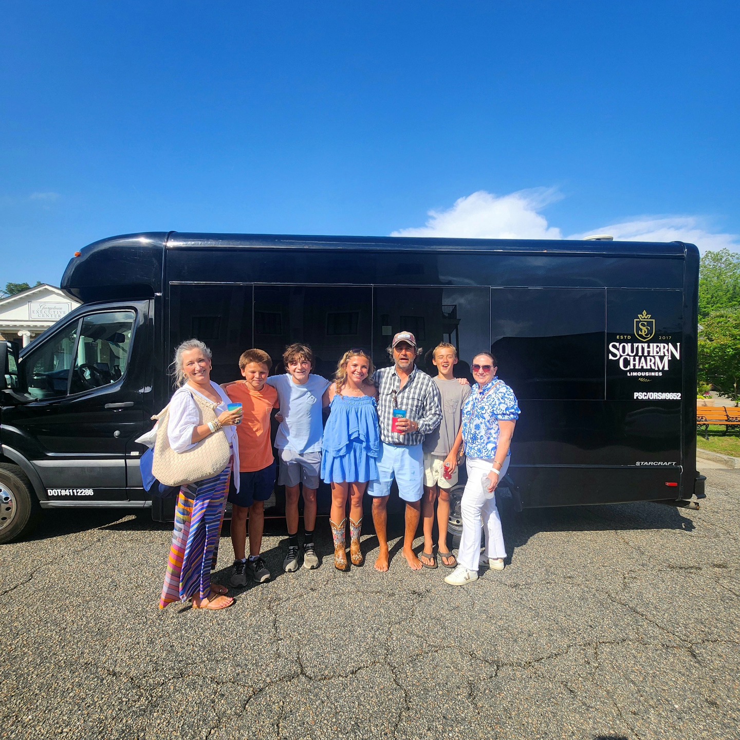 Family and friends in front of a black Southern Charm Limousines bus, ideal for Myrtle Beach airport transfer.