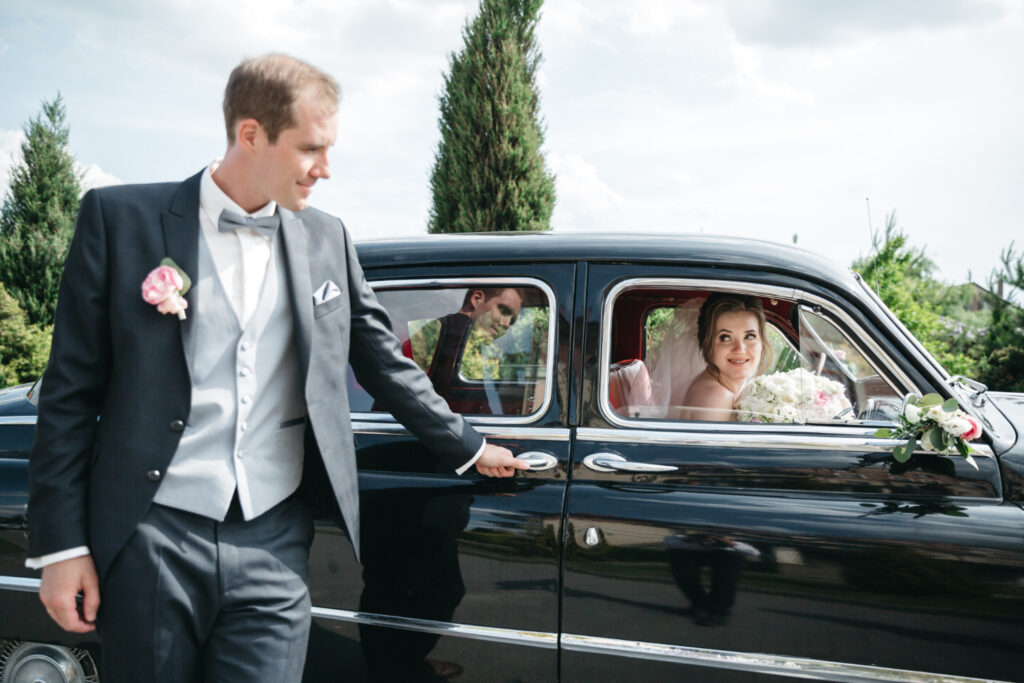 Groom opens car door for bride in wedding attire