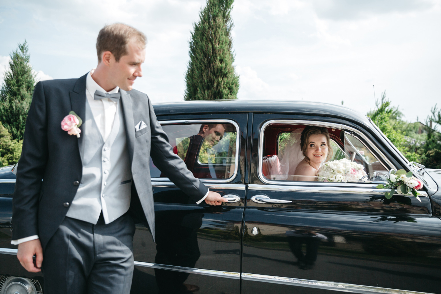 Groom opens car door for bride in wedding attire
