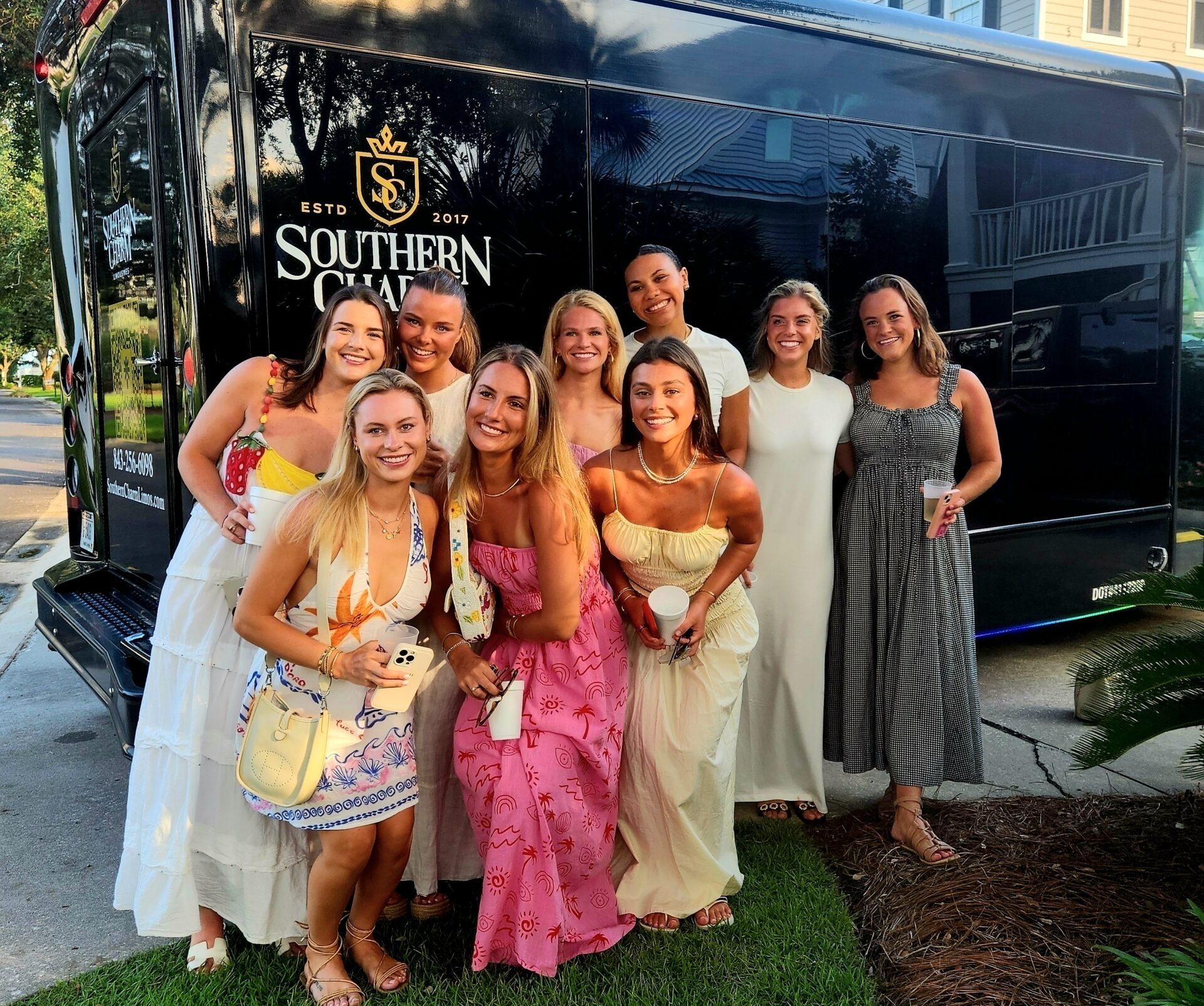 Group of women in dresses pose in front of a black Southern Charm bus