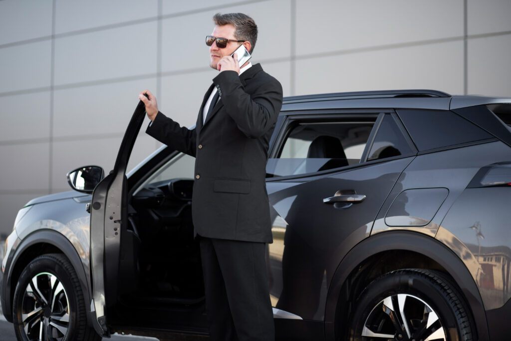 Man in suit on phone by car, discussing hourly corporate car service.