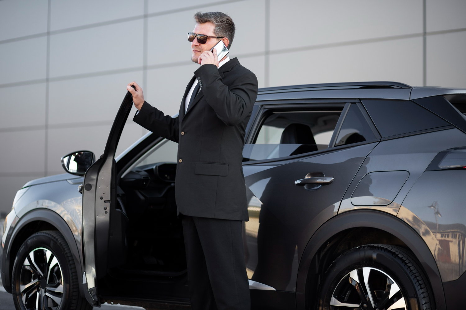 Man in suit on phone by car, discussing hourly corporate car service.